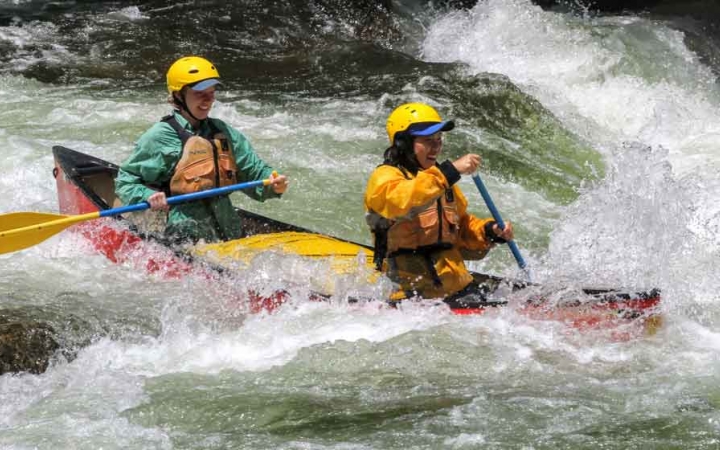 two students in a canoe navigate whitewater in north carolina on an outward bound trip